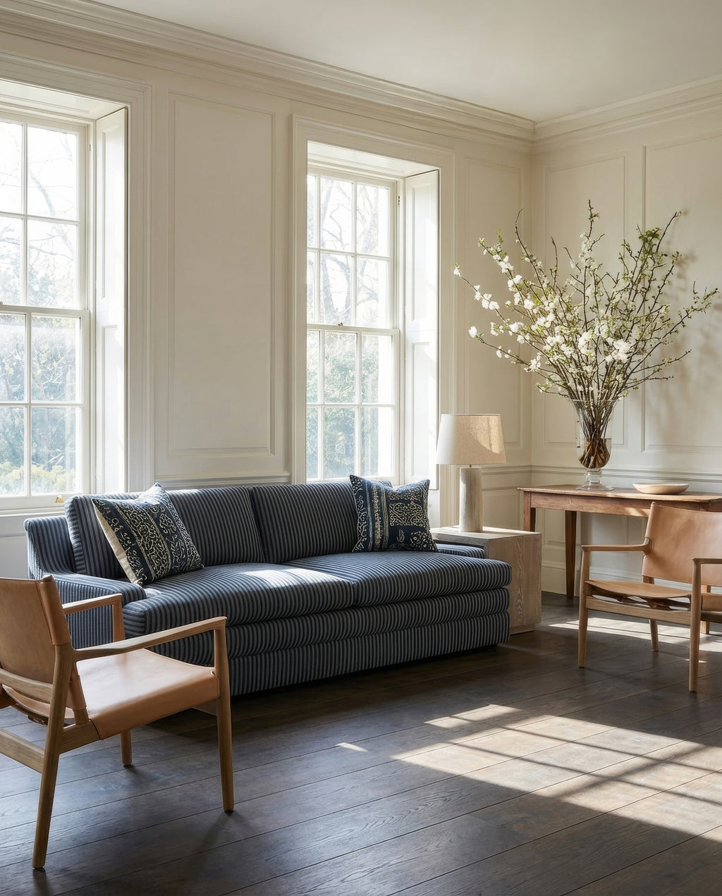 Living room with a blue striped sofa, wooden chairs, and a vase of flowers.